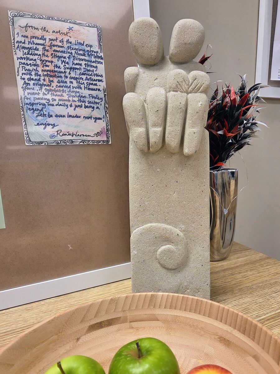 A carved stone sculpture of two figures embracing, with a handwritten note from the artist, on display at a Recovery Café